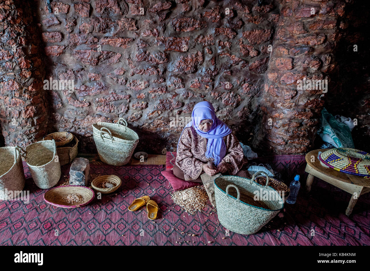 Olio di argan produzione. Una donna berbera rompere il guscio duro di un dado di argan con una pietra. Essaouira, Marocco Foto Stock