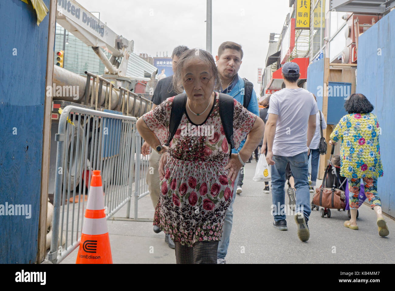 Una vecchia donna cinese camminando per strada principale con una forte espressione in Chinatown, lavaggio, Queens, a New York City. Foto Stock