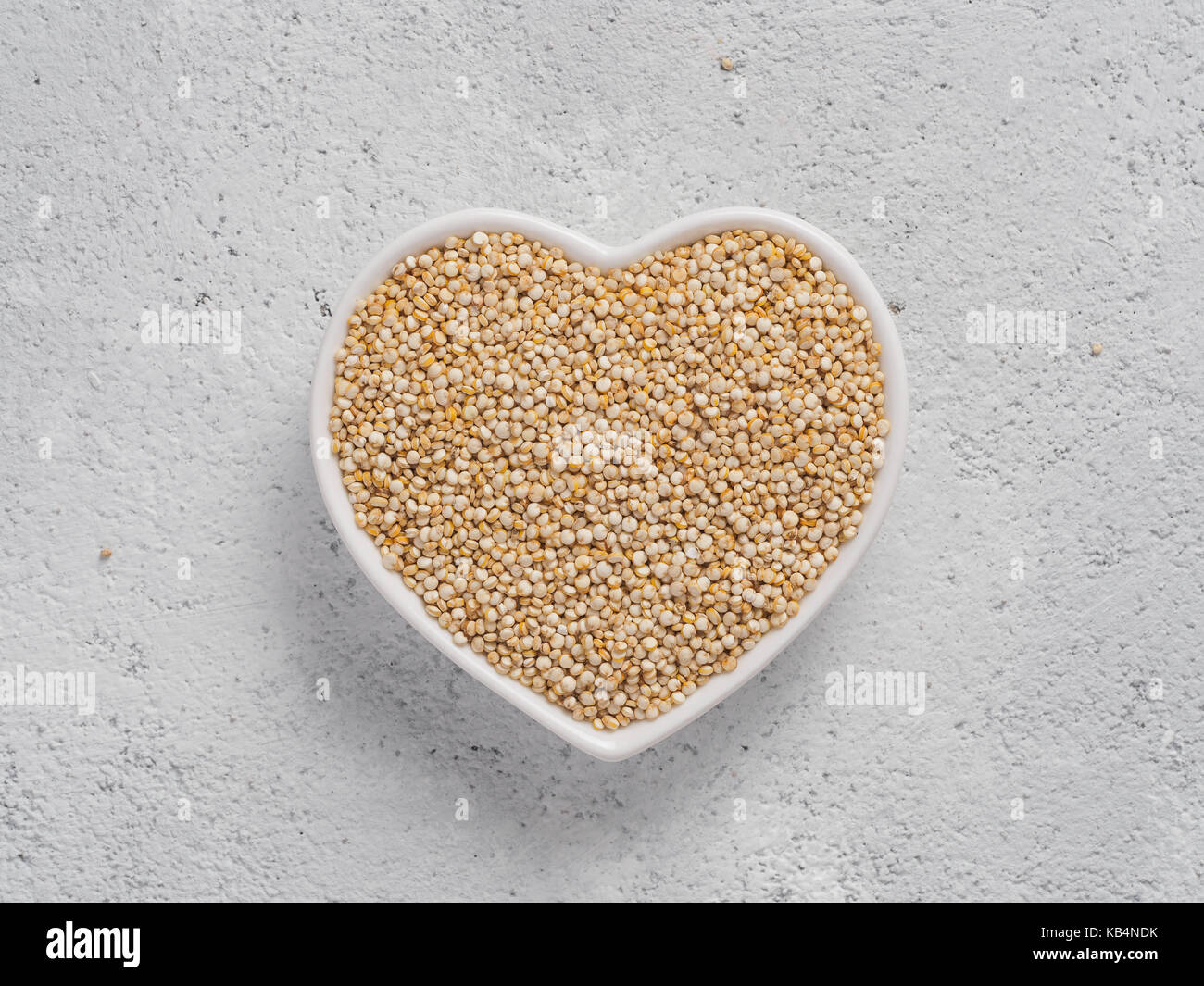 La quinoa nel cuore a forma di ciotola sul cemento grigio Sfondo. Senza glutine di grano antico per una sana dieta. Io amo la quinoa concetto. Copia dello spazio. Foto Stock