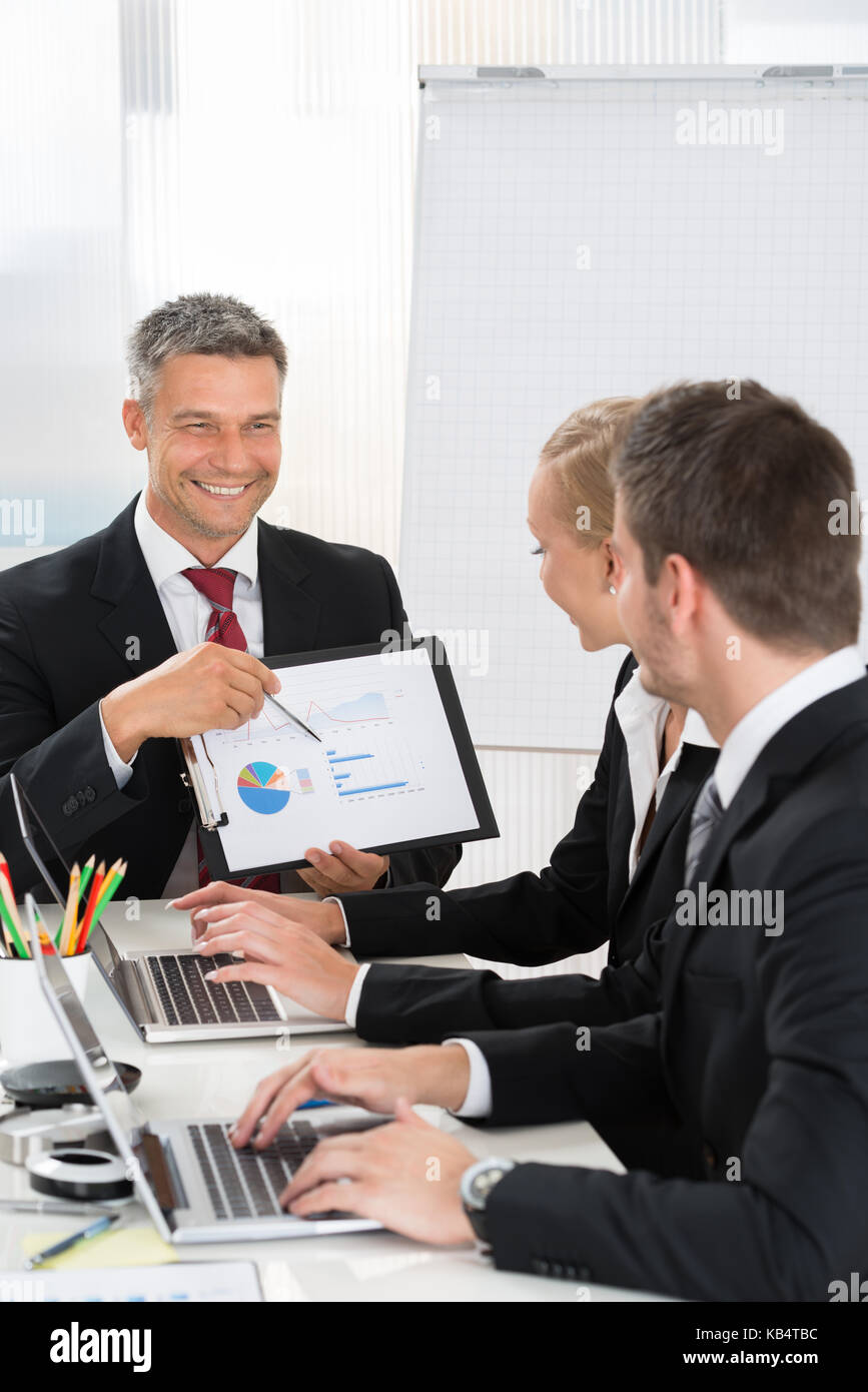 Imprenditore maturo che spiega il grafico ai suoi collaboratori in ufficio Foto Stock