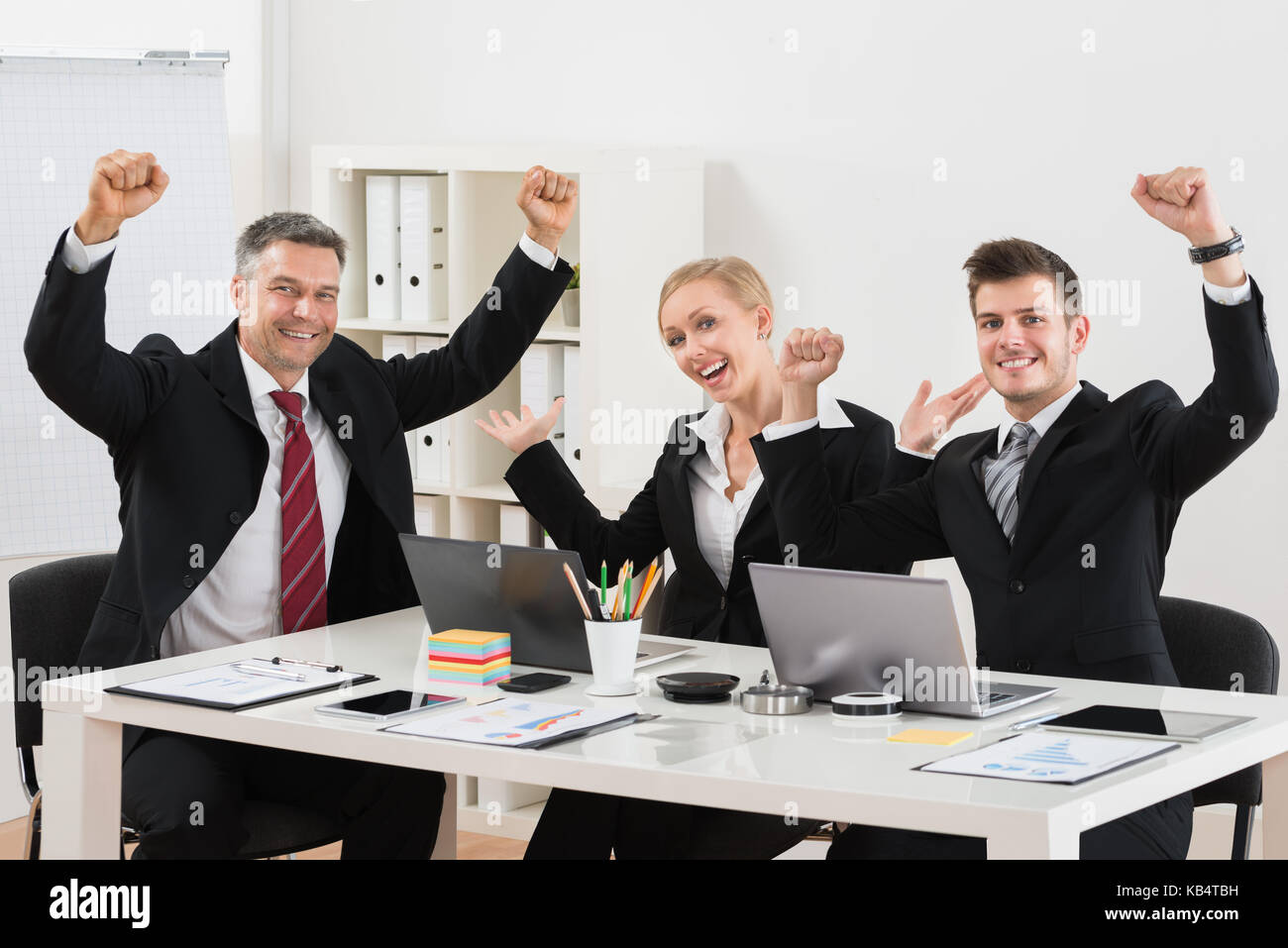 Gruppo di imprenditori felice con il braccio sollevato seduto alla scrivania Foto Stock