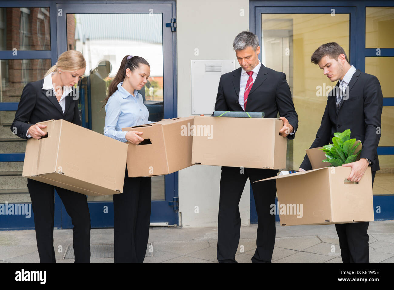 Gruppo infelice di operatori in piedi con le scatole di cartone al di fuori dell'ufficio Foto Stock