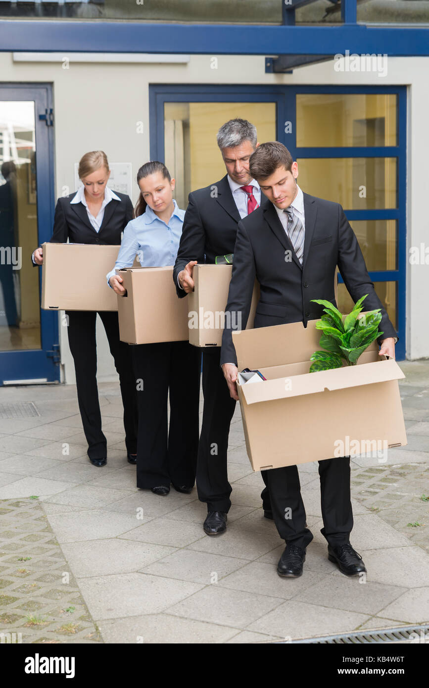 Deluso gli imprenditori in piedi in fila con scatole di cartone al di fuori dell'ufficio Foto Stock