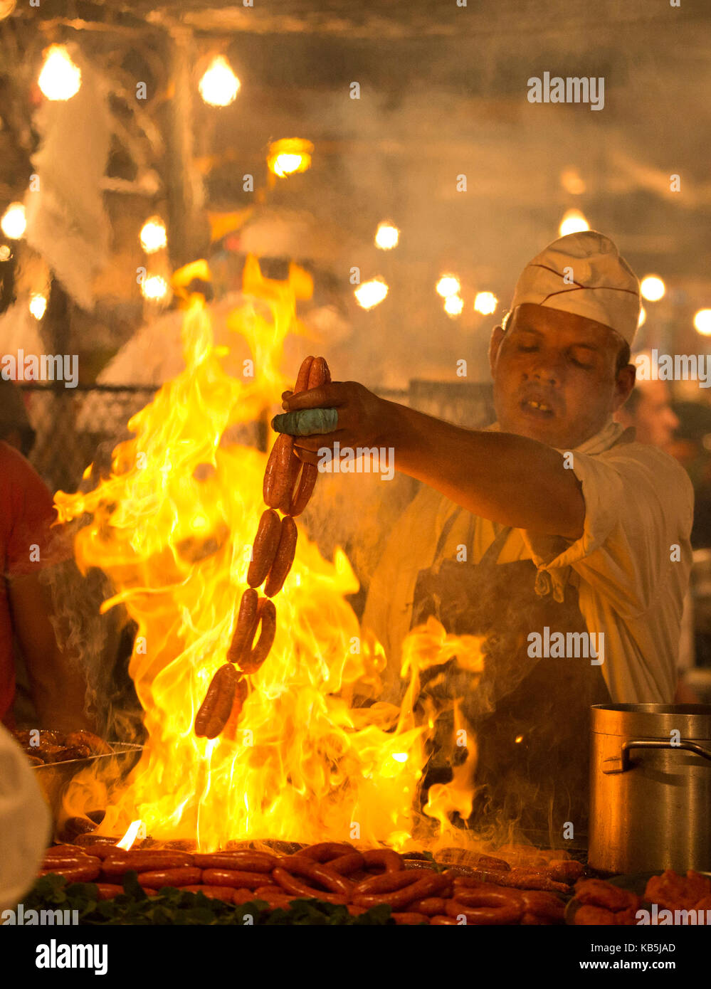 Uomo locale salsicce di cottura a fiamma viva in uno dei chioschi in Djemaa el Fna a Marrakech, Marocco, Africa del nord Foto Stock