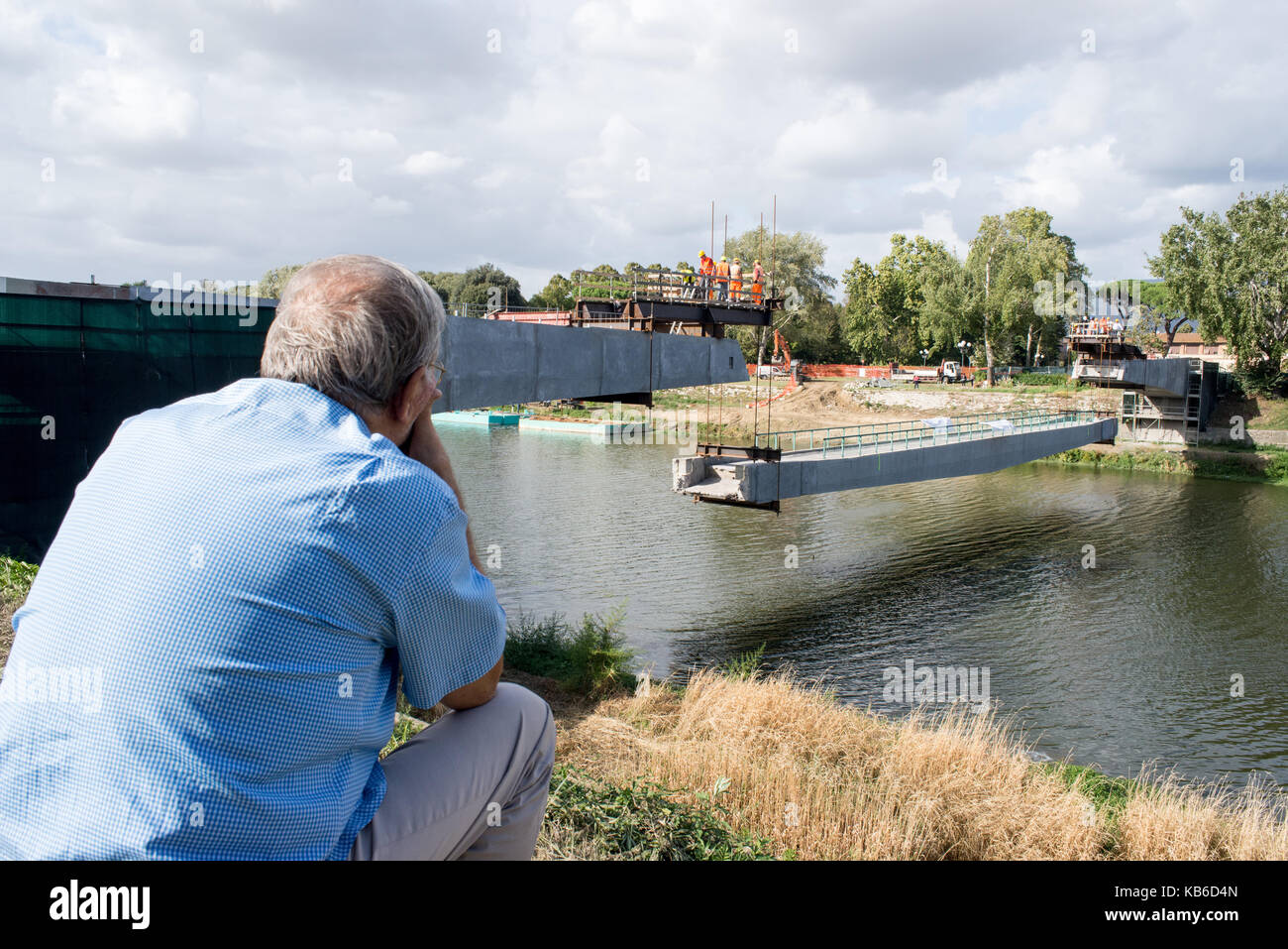 Un vecchio uomo guarda i lavori di ristrutturazione di un ponte di Firenze seduta su una panchina Foto Stock