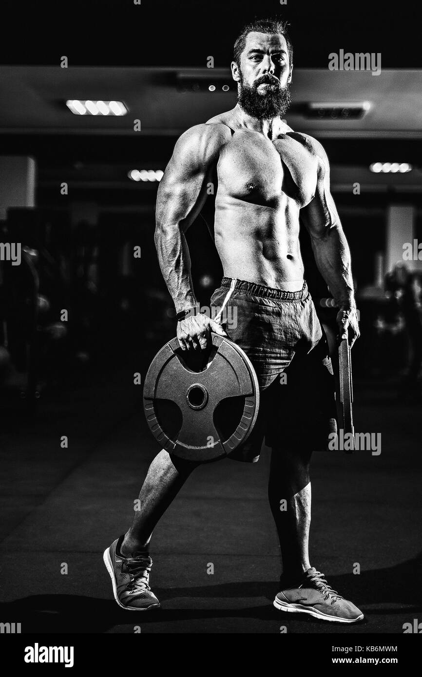 Atleta muscoloso bodybuilder uomo in posa con manubri in palestra. Foto Stock