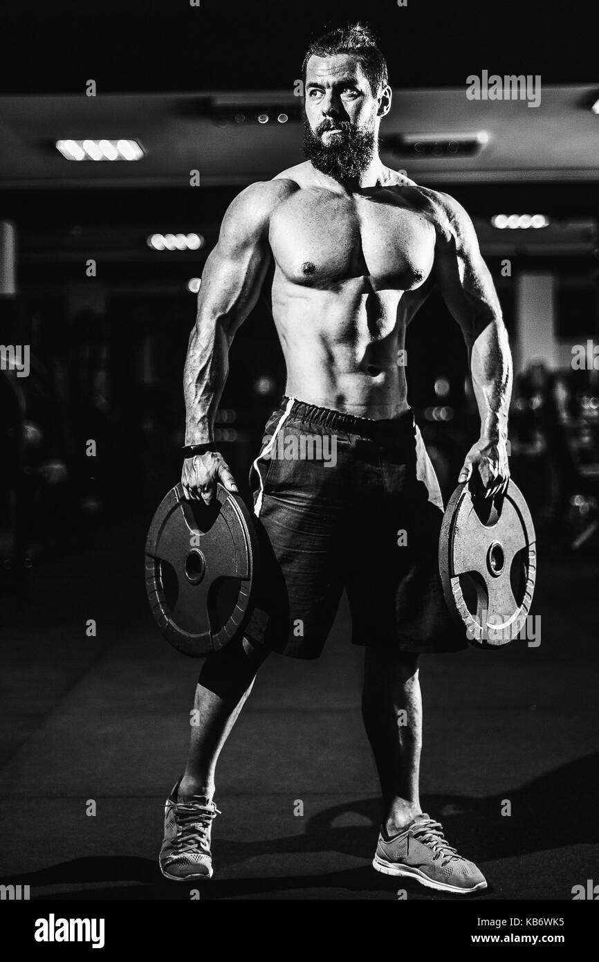 Atleta muscoloso bodybuilder uomo in posa con manubri in palestra. Foto Stock