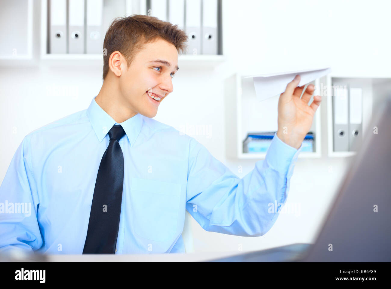 Ritratto di giovane imprenditore avviare un aeroplano di carta al suo luogo di lavoro in ufficio luminoso Foto Stock