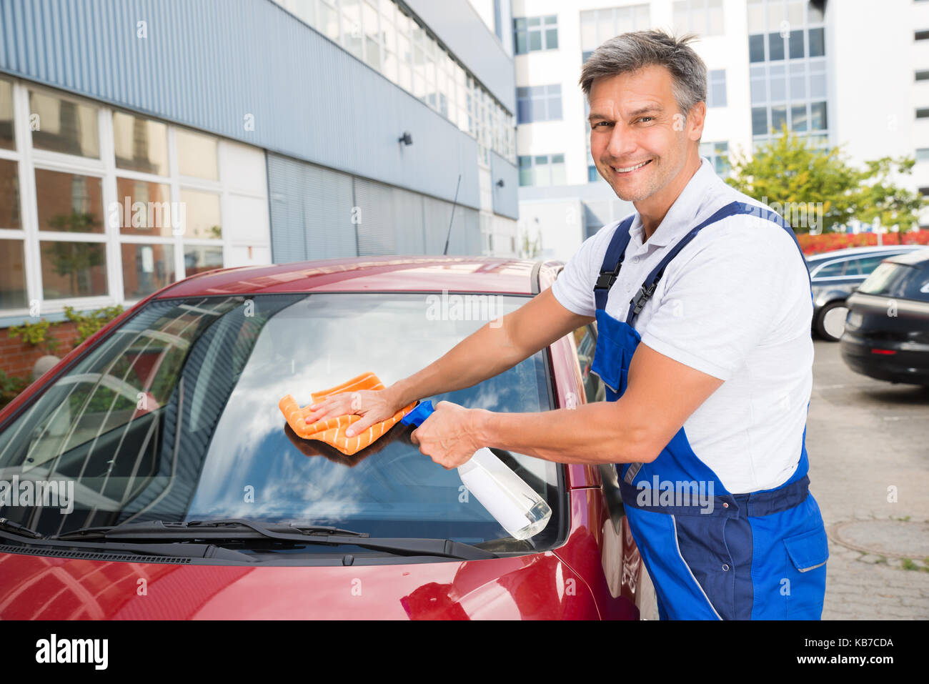 Maschio maturo lavoratore auto pulizia del parabrezza con un panno e la bottiglia spray Foto Stock