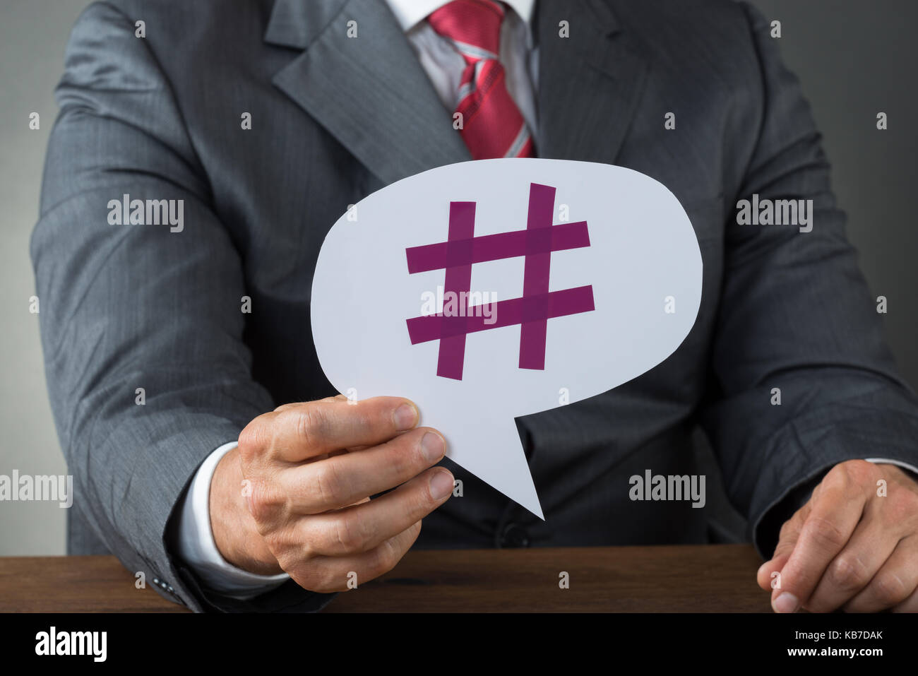 Sezione mediana di imprenditore che mostra hashtag su discorso bolla alla scrivania Foto Stock