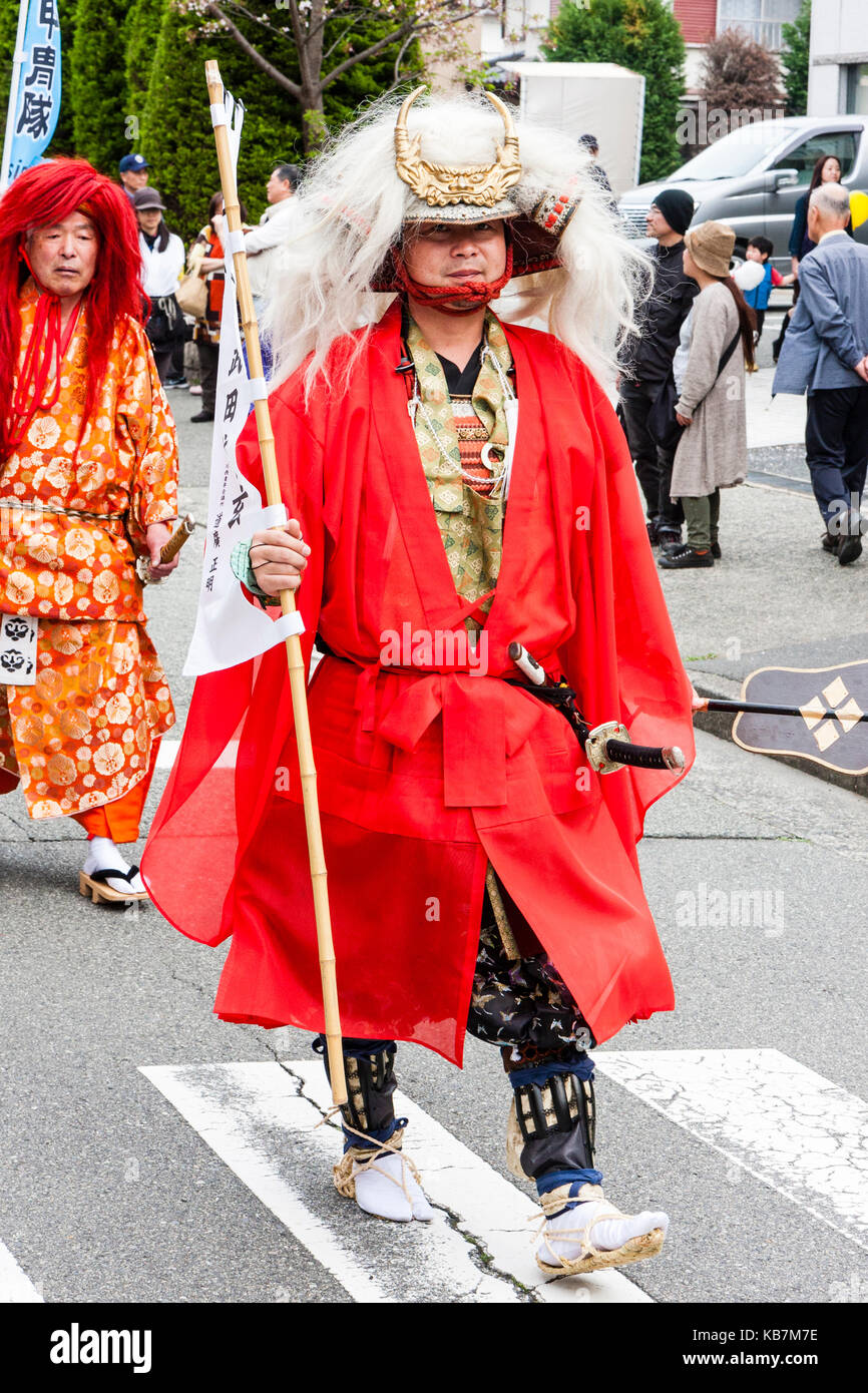 Annualmente Genji parade di Tada, Giappone. Samurai Warrior con lungo cappotto rosso e lunghi capelli bianchi sospesi dal casco crestato, camminando lungo la strada. Foto Stock