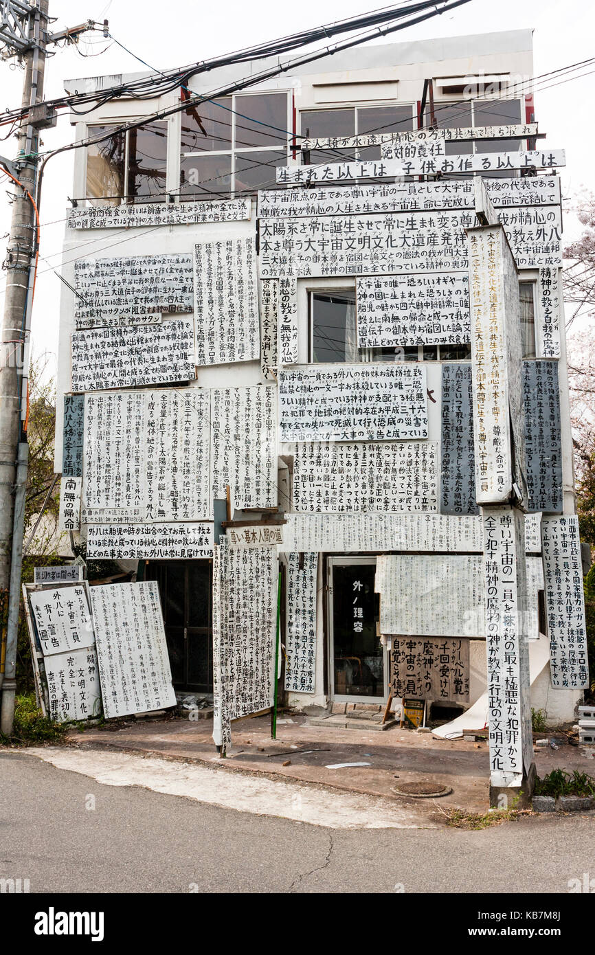 Giappone, Osaka, Tada. Tre storia house per la maggior parte coperta in bianco schede di protesta con la giapponese kanji script. Foto Stock