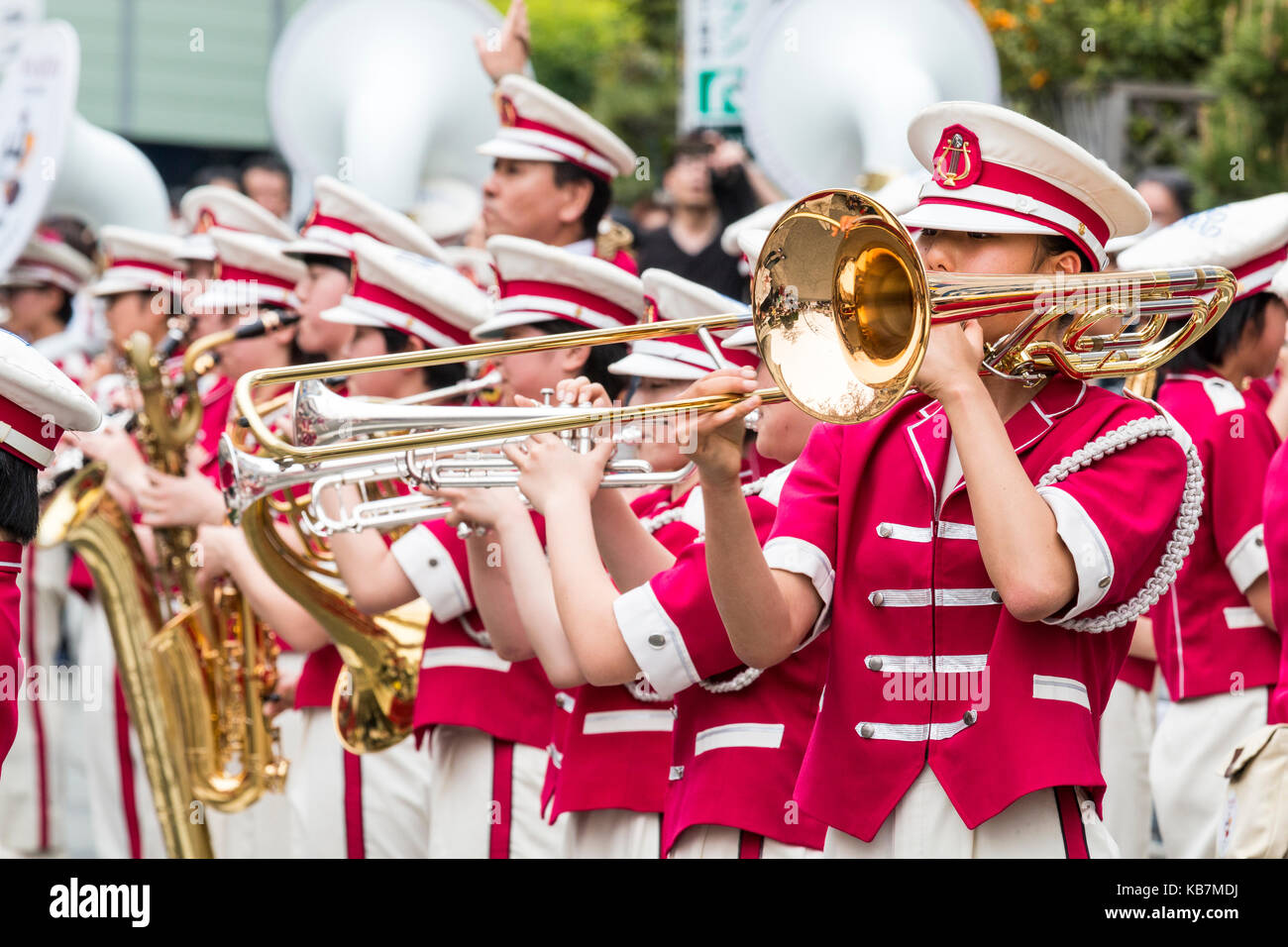 Giappone, Osaka, Tada. Genji parade. Banda femmina permanente attenzione alla riproduzione di tromboni e trombe. Vista guardando lungo. Divise rosa, bianco cappelli. Foto Stock