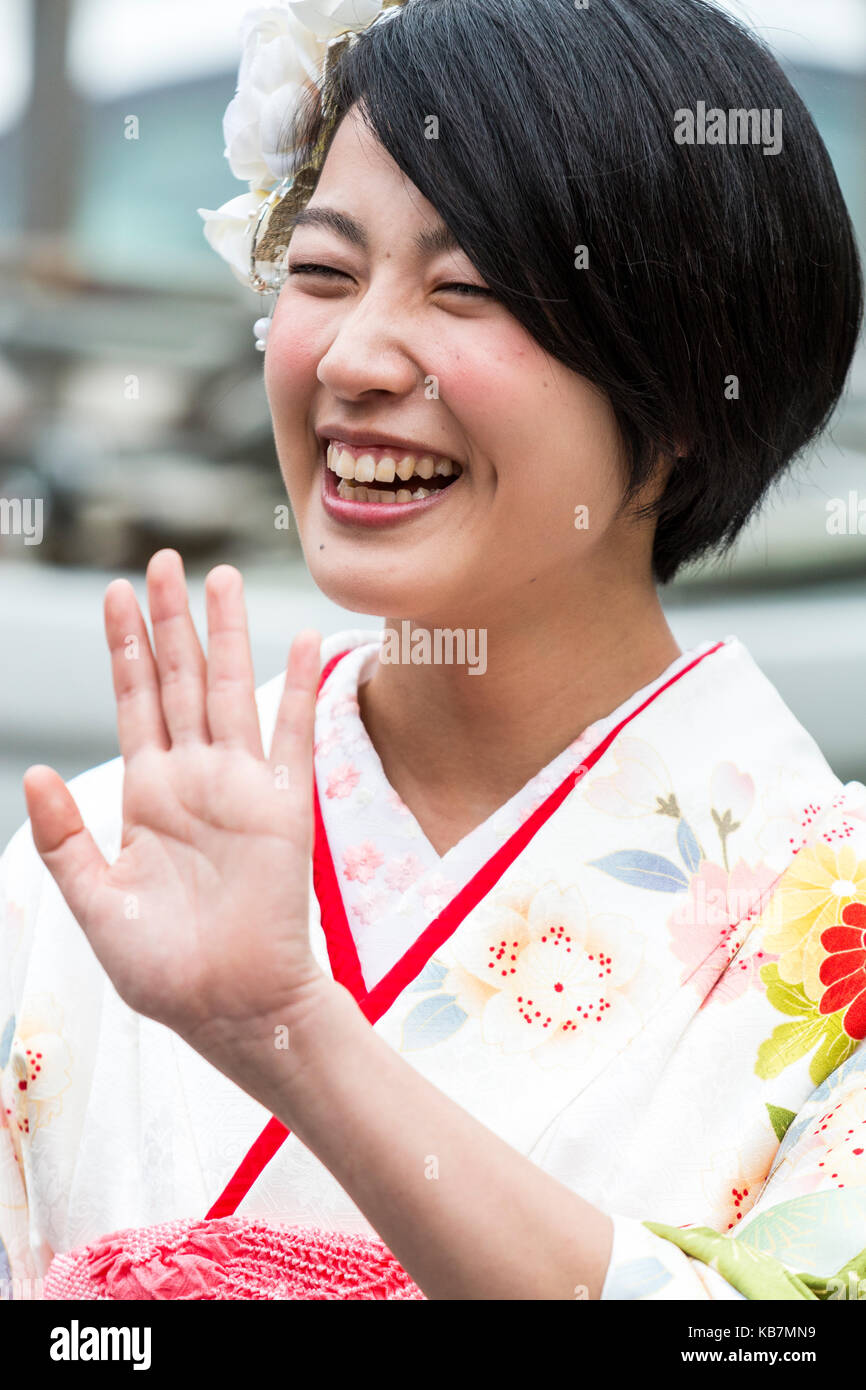 Il Giappone. Testa e spalle colpo di ridere giovane donna giapponese in color crema kimono. Bianco fiori nei capelli. Tenuto in mano fino a 'no stop' gesto. Foto Stock