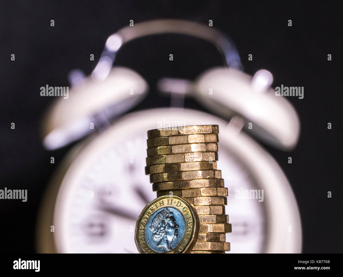 Defocalizzata orologio sveglia con nuovo cancelletto di monete. Concetto di legame tra il lasso di tempo e di denaro britannico / Regno Unito Sterline, eg termine finanziario / limite. Foto Stock