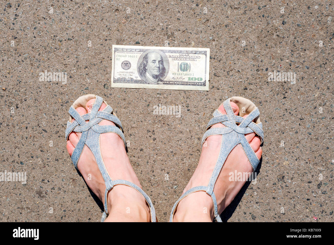 Lucky donna trovare i soldi per strada. donne piedi accanto a centinaia di dollari. Denaro smarrito e ritrovato sdraiato sulla strada asfaltata. Foto Stock