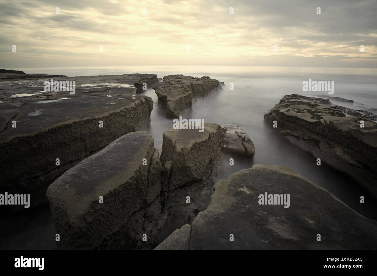 Una lunga esposizione seascape orizzontale del vulcanico costa rocciosa a san Diego in California presa al tramonto. Foto Stock