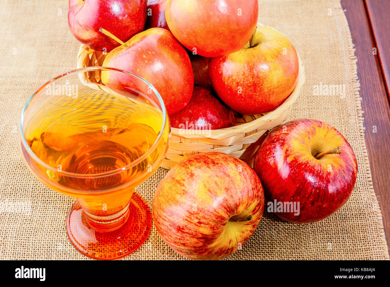 Sidro di mela in vetro e le mele rosse nel rustico cesto in vimini su sfondo di legno Foto Stock