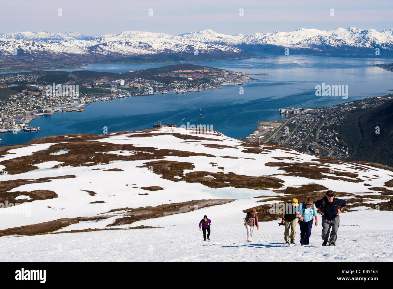 Gli escursionisti a piedi attraverso la neve sul monte Storsteinen con vista città sull isola Tromsoya in estate. Tromso, Troms, Norvegia e Scandinavia Foto Stock