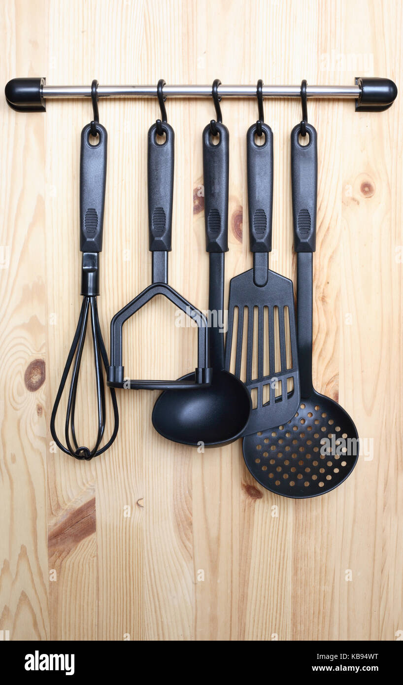 Set di moderno nero arnese da cucina appeso su sfondo di legno Foto Stock