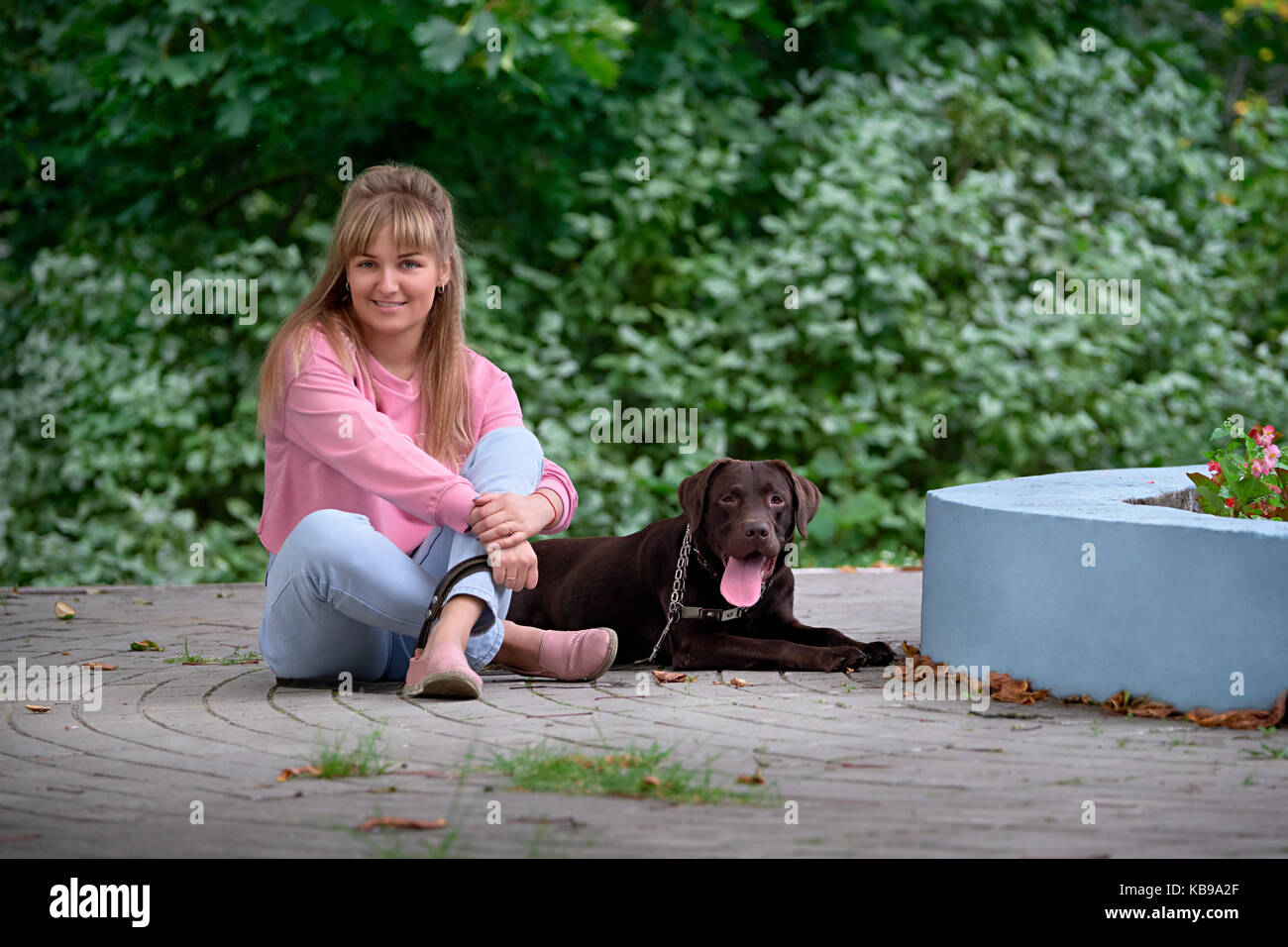 Ragazza bionda sorridente con cani Labrador. labrador che giace accanto Foto Stock