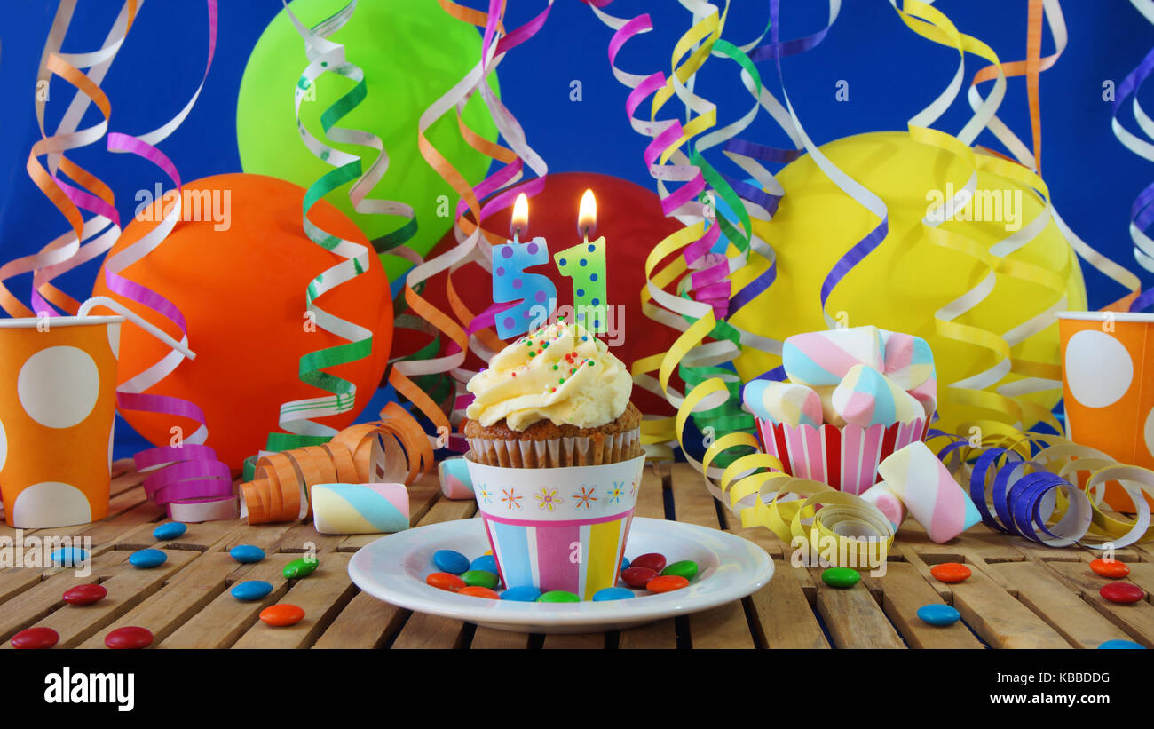51 compleanno tortina con candele accese sulla tavola in legno rustico con sfondo di palloncini colorati con bicchieri di plastica caramelle sulla parete blu in background Foto Stock