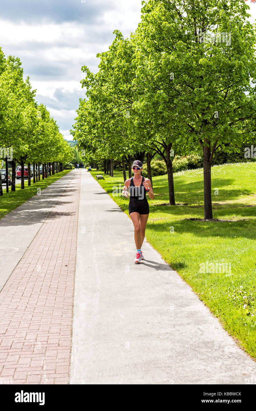 Saguenay, Canada - 3 Giugno 2017: Senior donna in esecuzione sul marciapiede sentiero nella città di Québec con alberi verdi in estate park Foto Stock