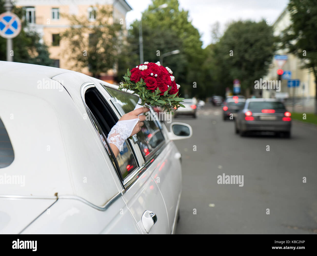 Unidentified sposa bloccato fuori la sua mano con il mazzo rosso dalla finestra del decorato bianco auto e leggermente sventolare su caldo giorno d'estate. Foto Stock