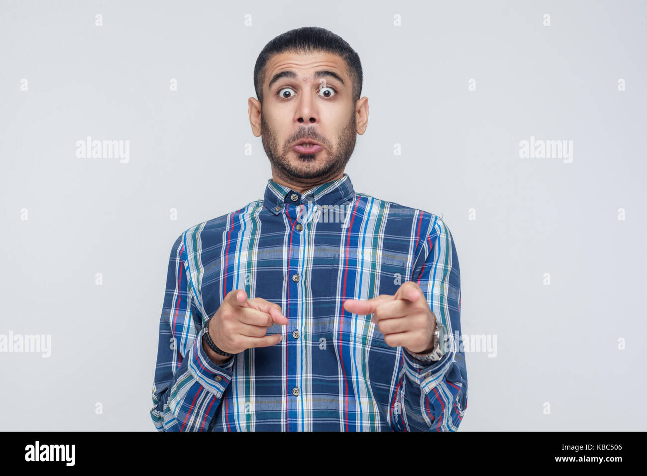 L'uomo seriosly, indossa una maglietta blu, bocche di apertura ampiamente, dopo aver stupito sconvolto guarda, puntare il dito alla telecamera. isolato studio shot su grigio b Foto Stock