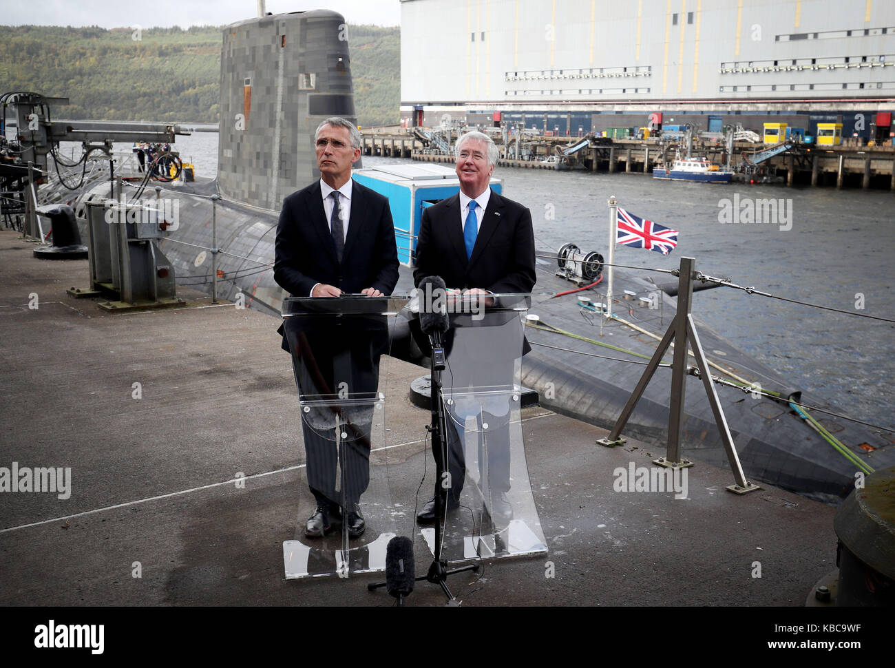 Il segretario alla difesa di sir michael fallon (a destra) e il segretario generale della NATO jens stollenberg (sinistra) parlare con i media a fianco della Vanguard-classe deterrente nucleare sommergibile hms vendetta durante una visita alla hm base navale clyde, faslane, dove i negoziati bilaterali sulla collettiva di sicurezza globale sono state detenute. Foto Stock