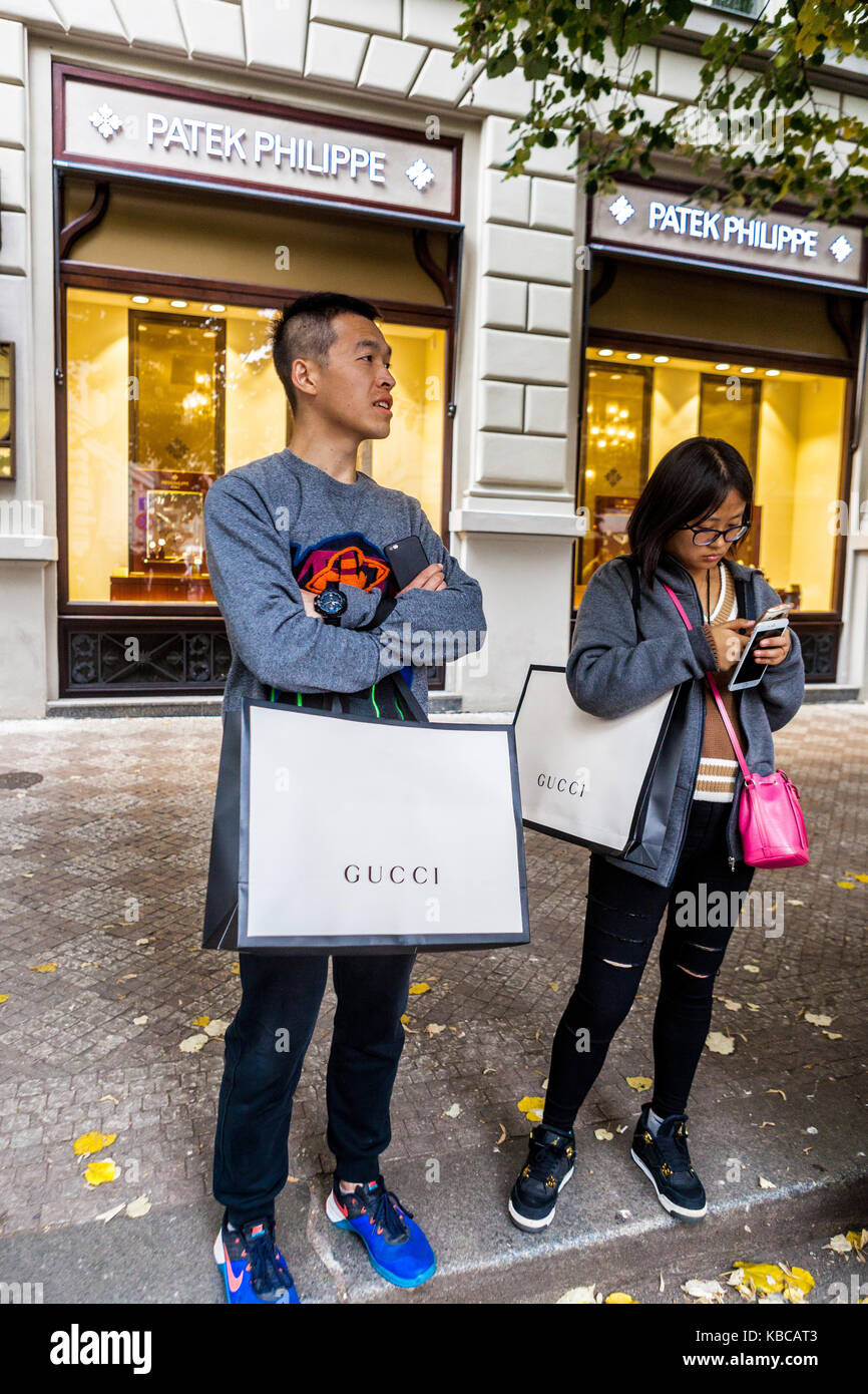 Via Parizska, shopping a Praga, turisti asiatici della Repubblica Ceca di fronte al lussuoso negozio Patek Philippe con borse di carta Gucci Foto Stock