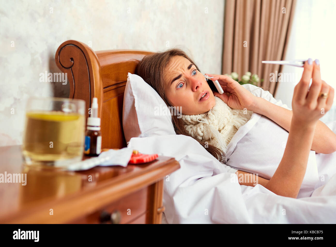 Una ragazza malata con un termometro sul letto chiama il medico su th Foto Stock