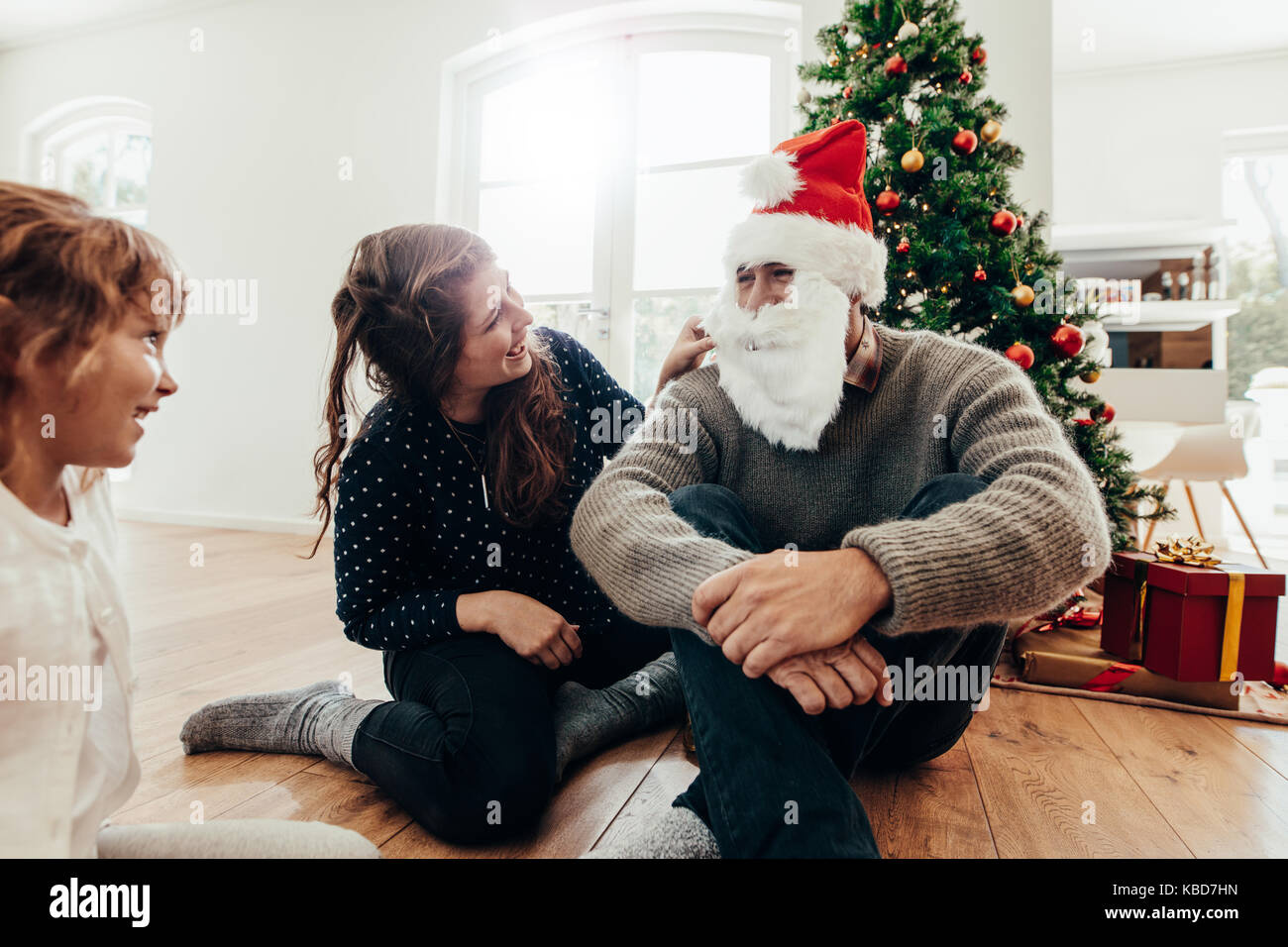 Famiglia festeggiano il Natale a casa con albero di Natale e regali. Donna e bambino guardando l uomo con Santa il cappello e la barba. Foto Stock
