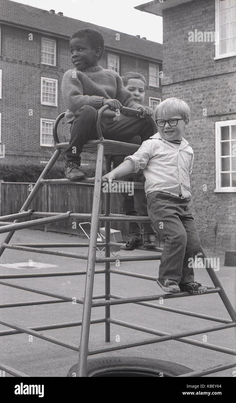 Anni Settanta, foto storiche di tre giovani ragazzi giocare insieme su un telaio di arrampicata in un vivaio parco giochi su un alloggiamento del consiglio estate in Deptford, nel sud di Londra, Inghilterra, Regno Unito. Foto Stock