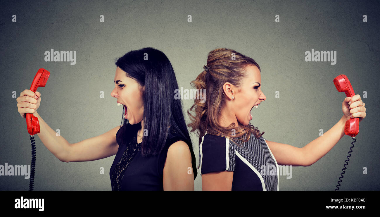 Concetto di comunicazione. due donne arrabbiato urlando a ogni altra al telefono isolato su sfondo grigio. Foto Stock