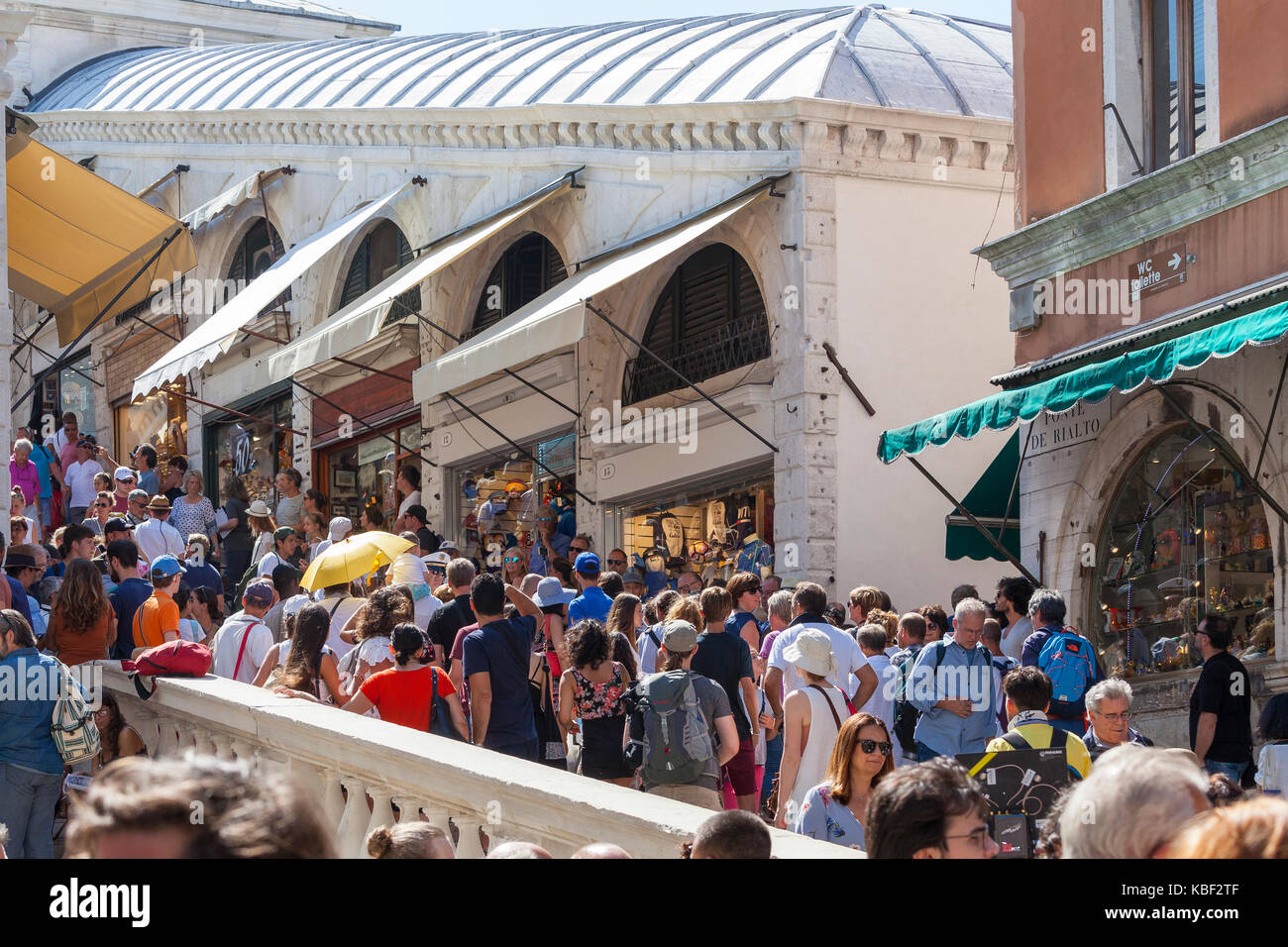 La folla di turisti assiepati i passi del Ponte di Rialto e San Marco, Venezia, Italia davanti alla fila di piccoli negozi come tentano di attraversare th Foto Stock