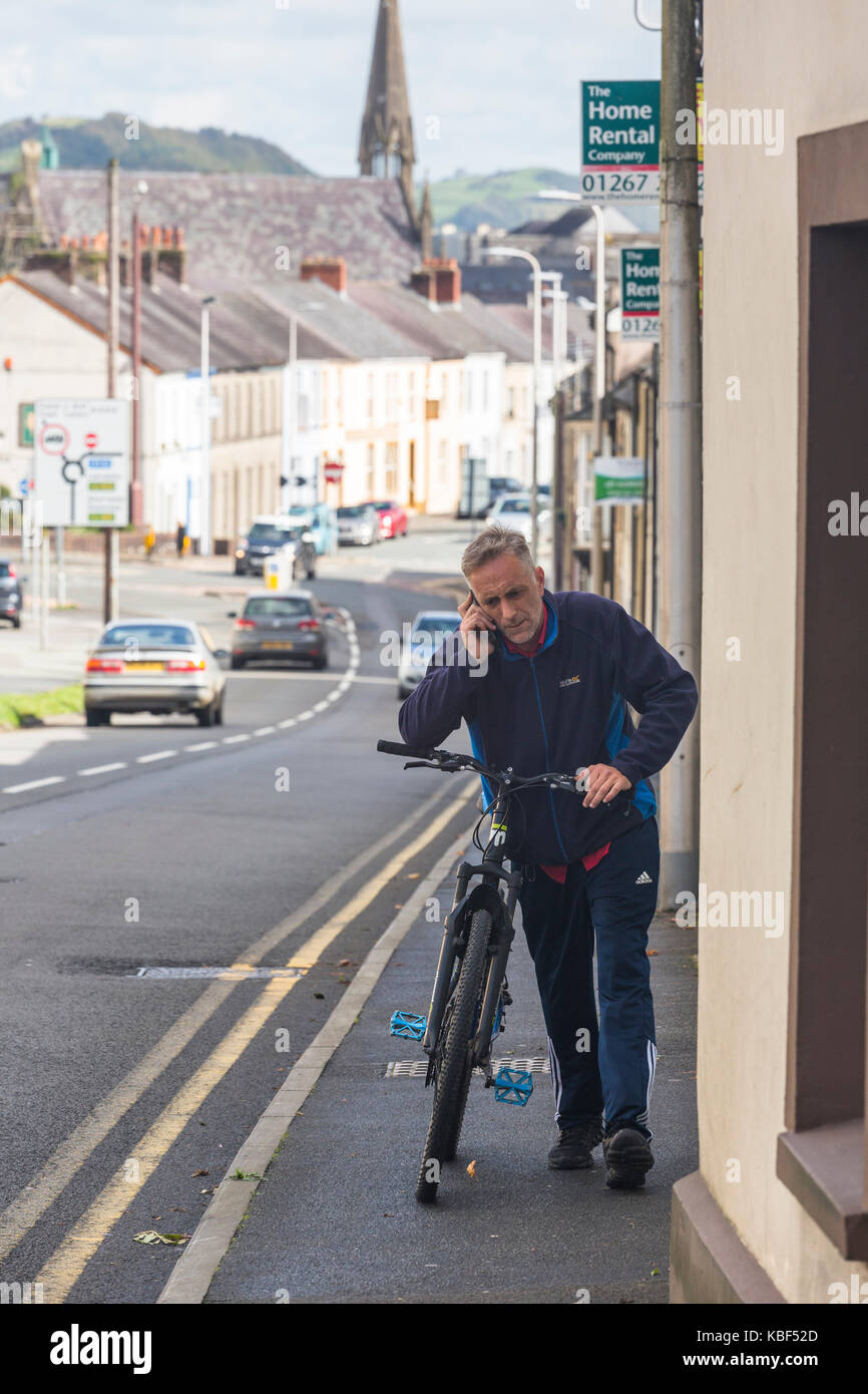 Uomo che parla su telefono cellulare mentre la bicicletta di spinta lungo il marciapiede in città Foto Stock