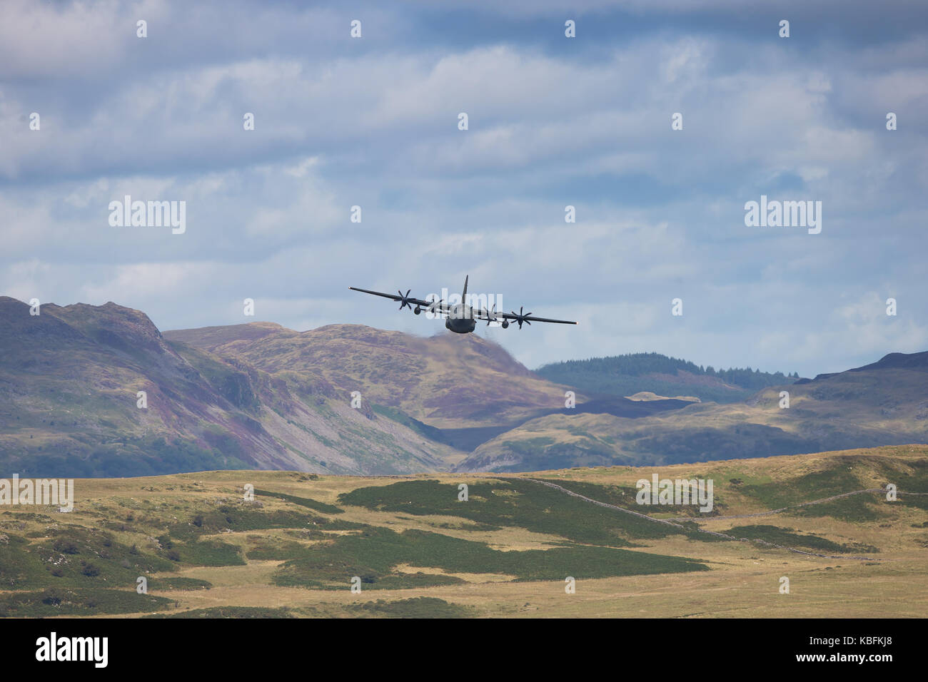 Un basso-battenti Hercules la rotta del velivolo verso la fotocamera; Welsh montagne sullo sfondo & cielo nuvoloso creare spettacolare sfondo. Mid-Wales, UK. Foto Stock