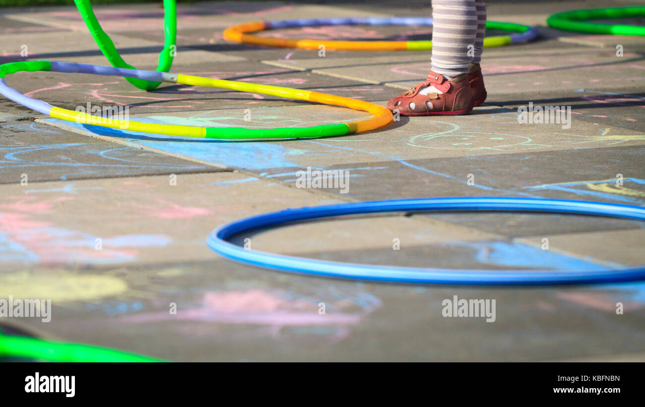 Piccola ragazza giocare hula hoops sul parco giochi graffiato con Chalk. Foto Stock