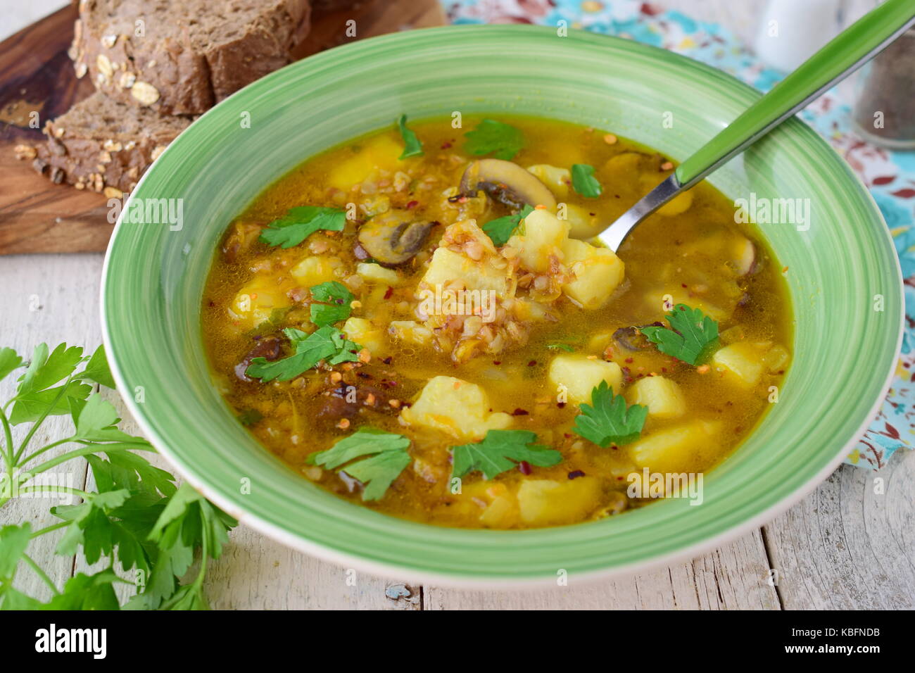 Una sana zuppa di grano saraceno, di fecola di patate, i funghi, la carota e la cipolla wit di olio di oliva in una ciotola verde su uno sfondo di legno. Foto Stock