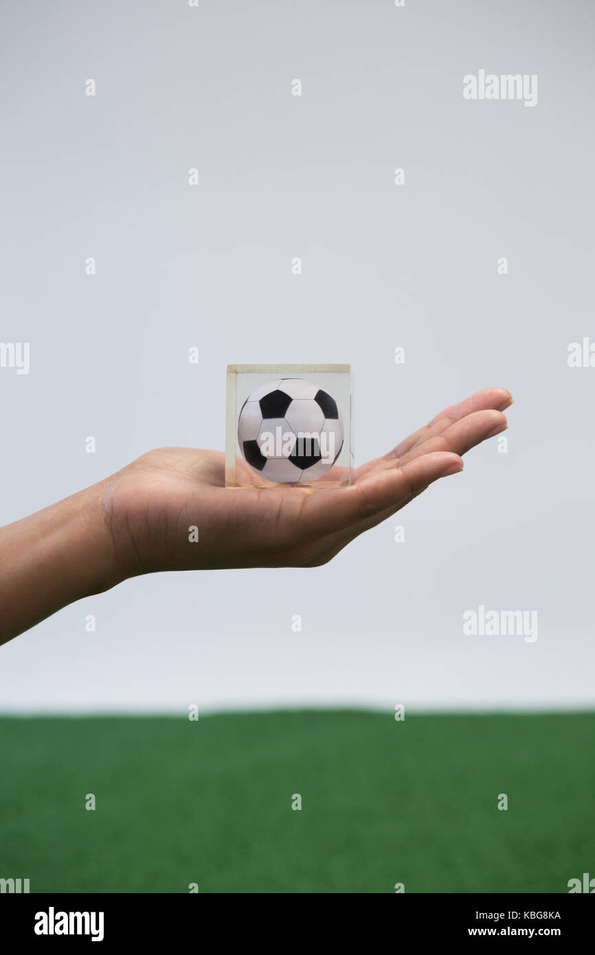 Close-up di mano azienda acrilico cubo di calcio contro uno sfondo bianco Foto Stock