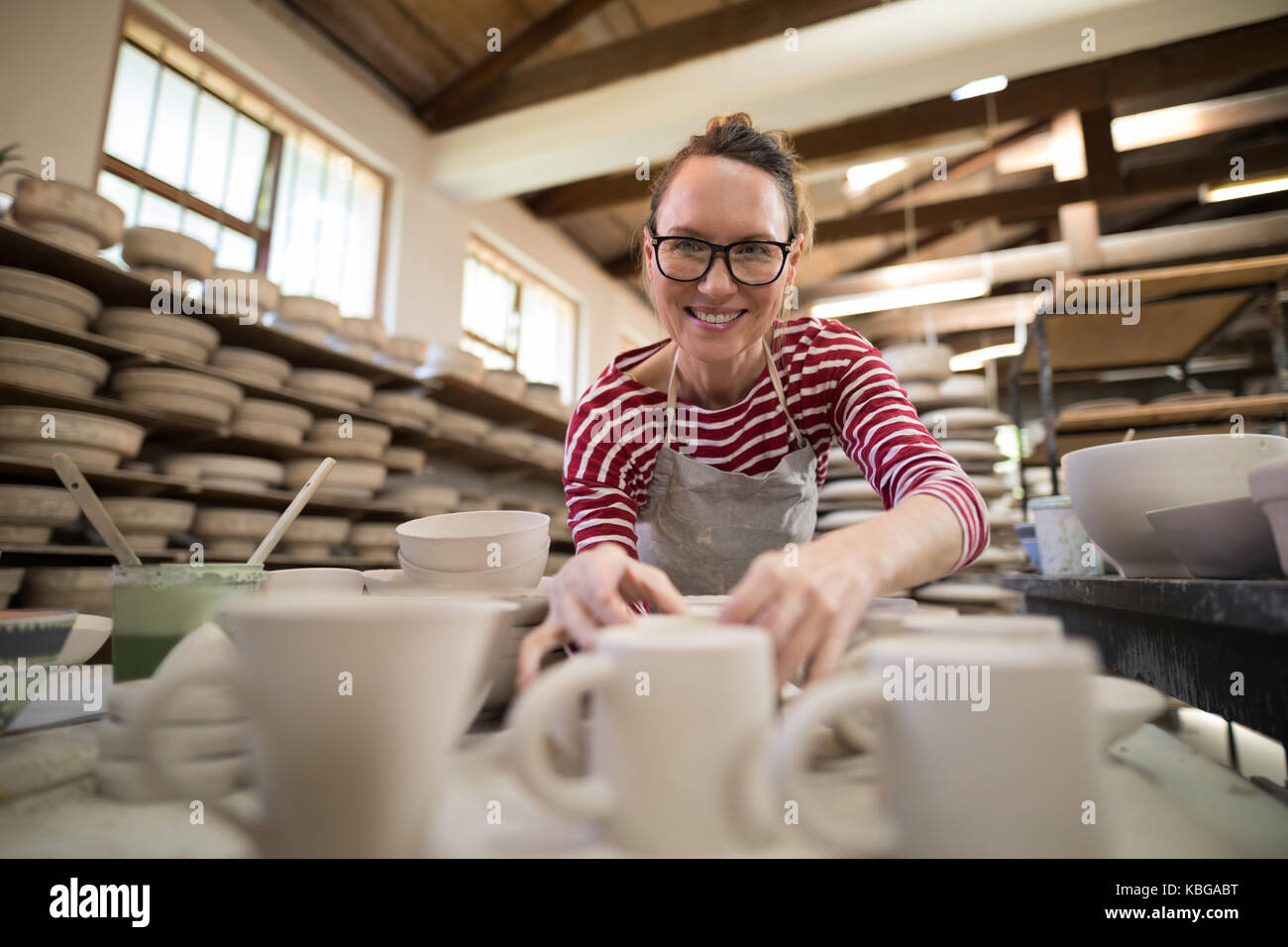 Ritratto di donna controllo tazze in corrispondenza del piano di lavoro nel laboratorio di ceramica Foto Stock