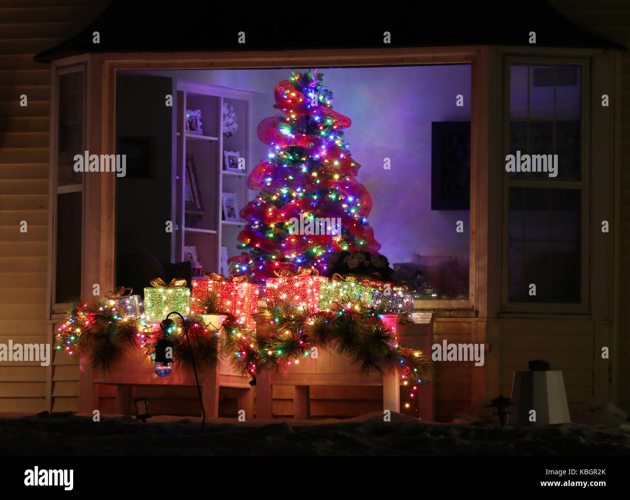 Finestra decorata con incandescente albero di Natale all'interno di una casa e luminose decorazioni per esterni, scena notturna, leggera sfocatura. Natale e Anno Nuovo vacanze b Foto Stock