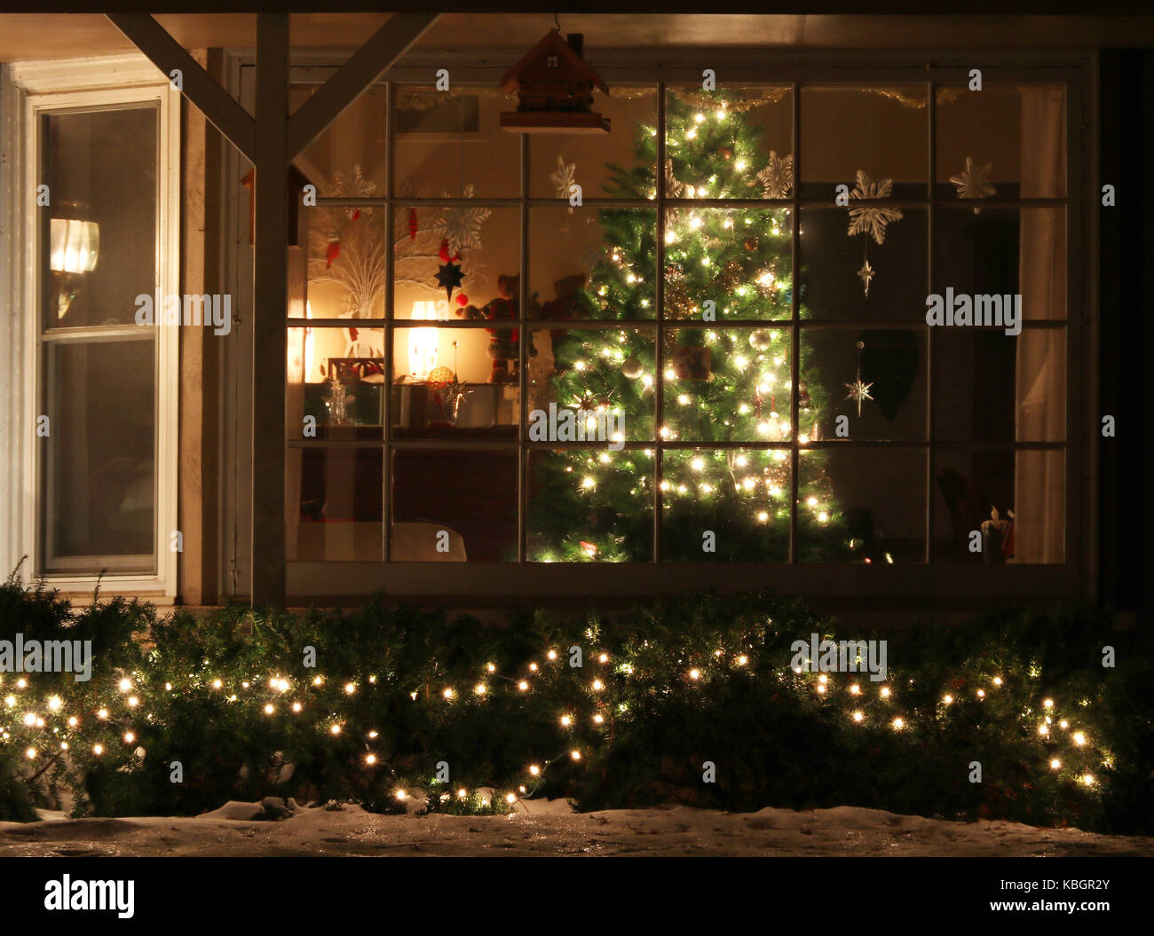Finestra decorata con incandescente albero di Natale all'interno di una casa e luminose decorazioni per esterni, scena notturna, leggera sfocatura. Natale e Anno Nuovo vacanze b Foto Stock