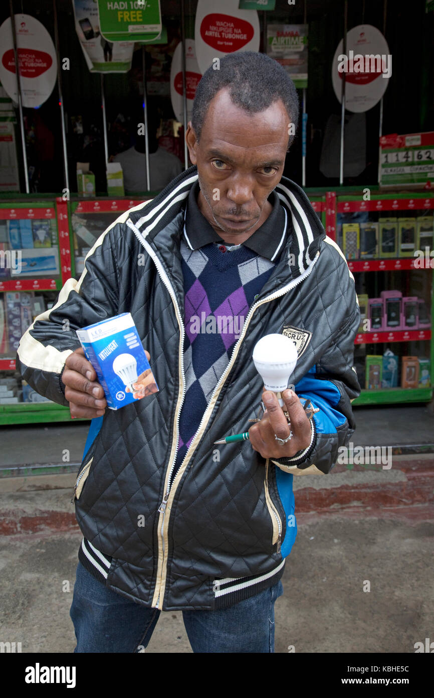 L'uomo africano holding energia effiecient lampade led esterno duka in kamere township kenya Foto Stock