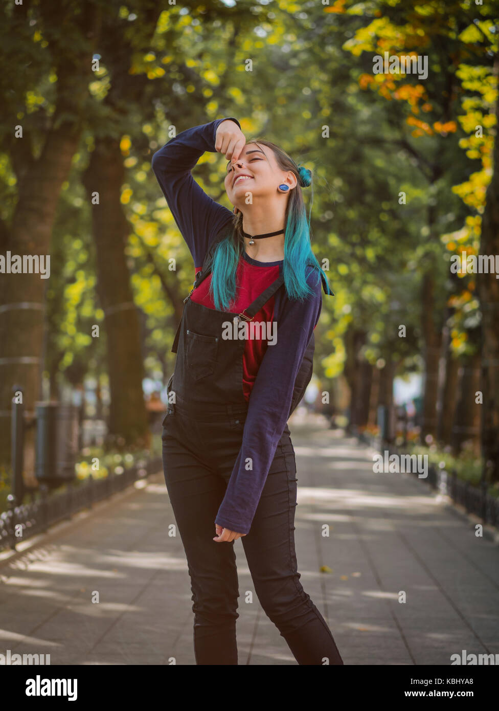 Street punk o hipster ragazza godendo di svuotare il vecchio parco europeo. ritratto di teen ragazza con blu capelli tinti,piercing nel naso,lenti viola e insolito hai Foto Stock