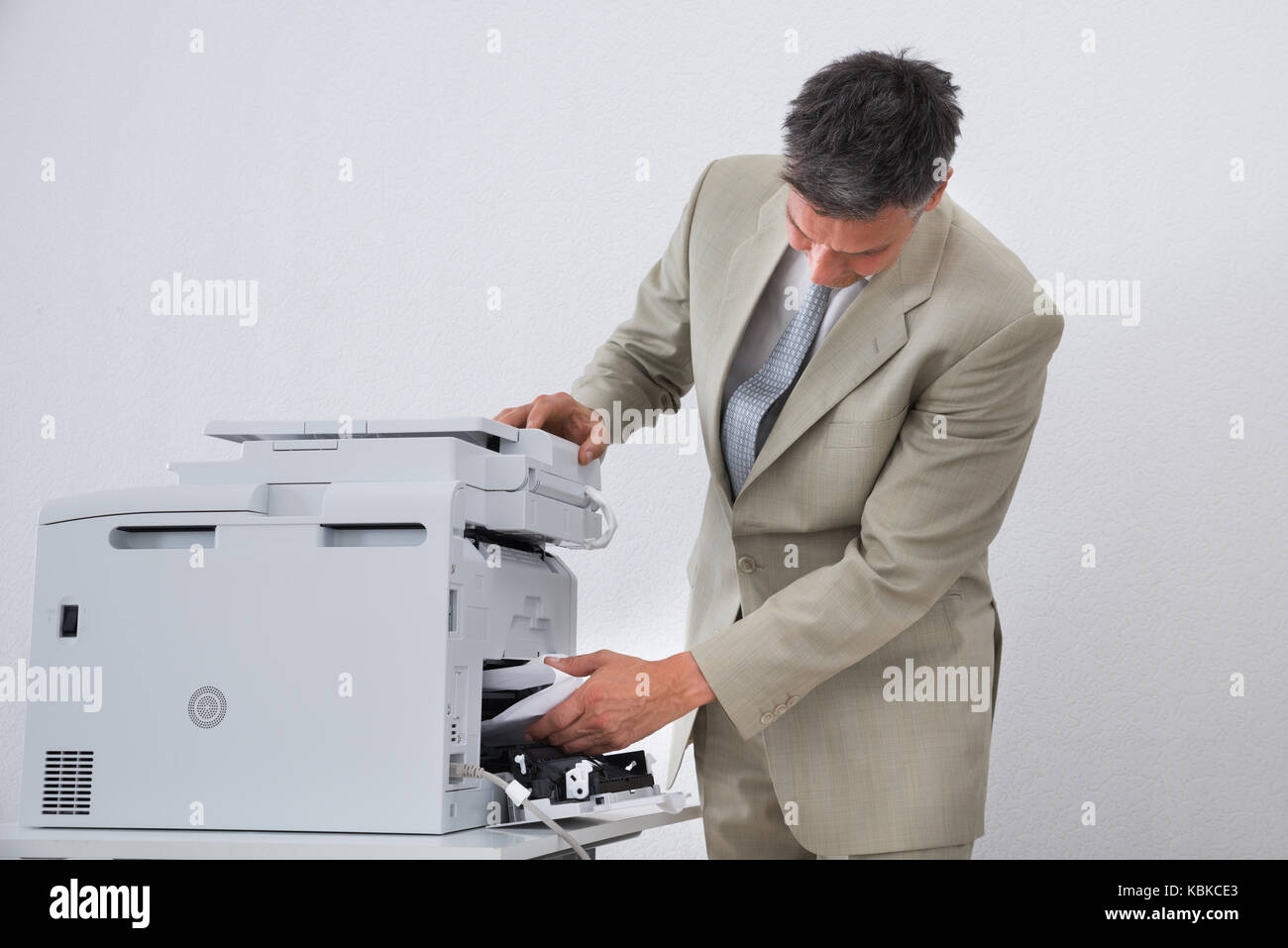 Imprenditore maturo di rimuovere la carta bloccata nella stampante in ufficio Foto Stock