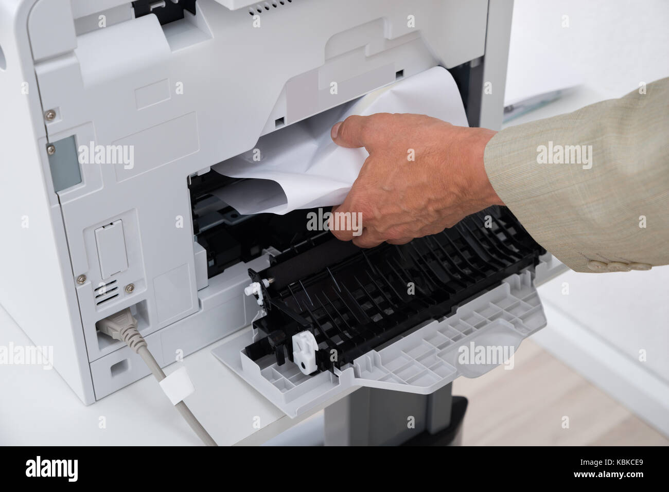 Immagine ritagliata di imprenditore il canto di rimuovere la carta bloccata nella stampante in ufficio Foto Stock