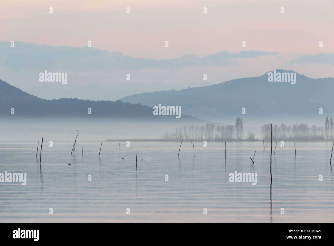 Il lago al tramonto con nebbia e bella, morbide e colori caldi e pali di legno in primo piano Foto Stock