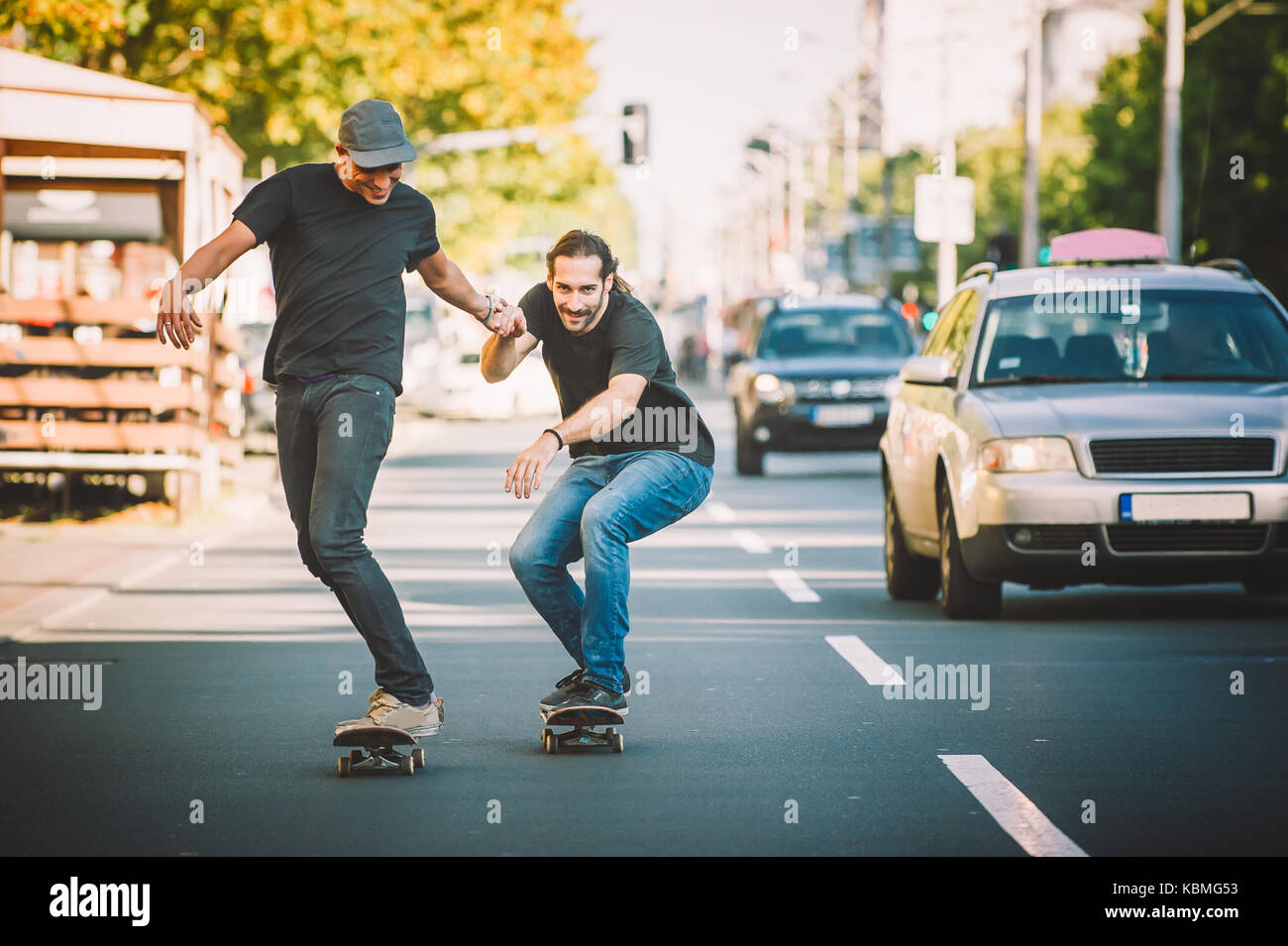 Due skateboard pro rider giro pattinare nella parte anteriore della vettura sulla città strada attraverso il traffico Foto Stock